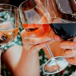 3 wine glasses filled with white, rose and red wine in a 'cheers' position over a table.