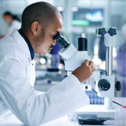 A person wearing a lab coat looking through a microscope