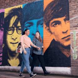 Two people walking past a mural of The Beatles.