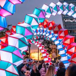 Accordion shaped archways in lots of colours, lit up with people walking through them