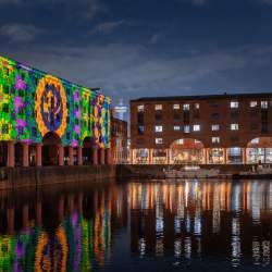 inside the Royal Albert Dock at night time with a colourful projection on the warehouse buildings