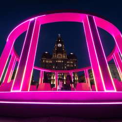 People inside a pink recreation of the eurovision stage on Liverpool Waterfront with the Liver Building in the background