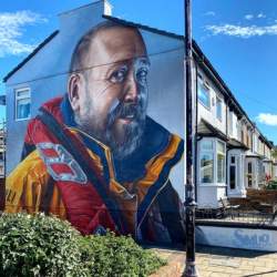A life like street art image of a coastguard worker on the side of a house in Wirral