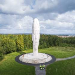 A statue of a head in white with grass and trees surrounding the sculpture.