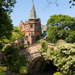 A red brick church and bridge surrounded by large, green trees