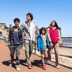 A family of four walk along a pier by Fort Perch Rock on a sunny day