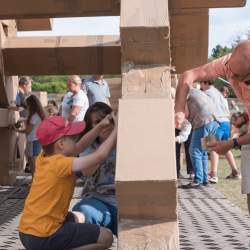 A grandfather and young boy working together with lots of other people to build a large cardboard structure in a park