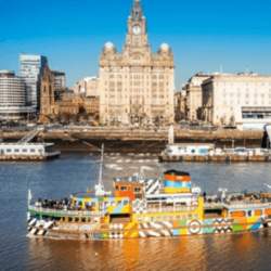 A colourful and patterned ferry on the Mersey River in the sunshine with the Royal Liver Building in the background