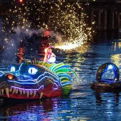 A dragon puppet on the water with fairy lights and