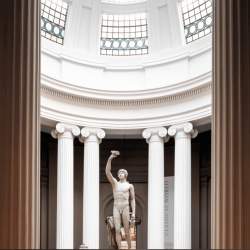 A white sculpture of a naked man inside a Grecian, domed building