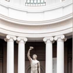 A sculpture of a male in a domed, Grecian style building with natural light pouring in