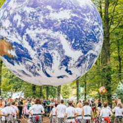 A crowd of people assembled in the forest under a large model of Earth, suspended in the trees