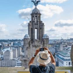 A man taking a photo of the Liver bird in the distance.