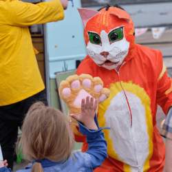 A person in a ginger cat costume high fives a young girl using their big cat paw