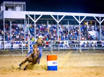 A barrel racer rounds a red, white, and blue barrel in front of a full stadium at the Iron County Fair in Parowan, Utah.