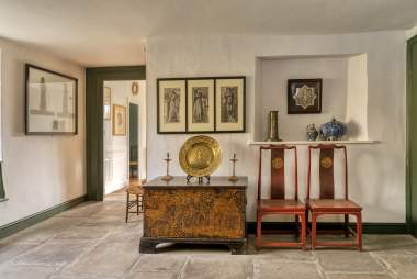 The Garden Room at Kelmscott Manor with William Morris artefacts in view: two Arts & Crafts chairs beside a chest and drawings on the wall