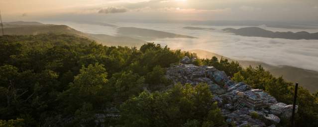 Sunrise over the Appalachian Mountains from Dan’s Rock Scenic Overlook in Dans Mountain State Park, with a rocky viewing platform surrounded by forest and a valley filled with morning fog.