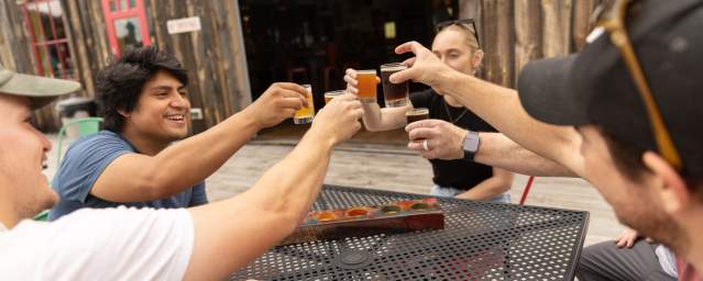 A group of adults sit around a table, holding up glasses of beer to cheers eachother.