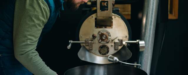 A man pulls a handle on a large coffee roaster machine.
