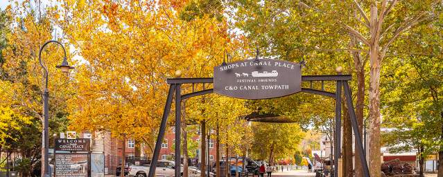 An archway over a stone and bricked path with full trees in fall colors in the background.