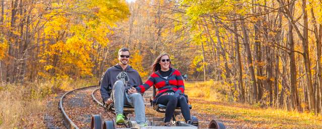 A couple peddles on a rail bike riding along the rail line in the fall.
