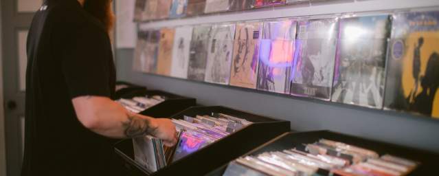 A man stands in front of a display, looking through a box full of vinyl records.