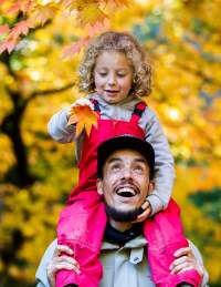 A man with a girl on his shoulders walking through the grounds of Westonbirt Arboretum near Bristol in autumn - credit Johnny Hathaway