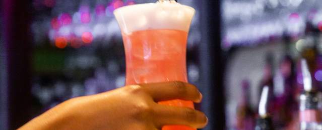 Hand holding a tall pink cocktail in front of the counter at Darryl's Corner Bar and Kitchen