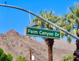 Green Palm Canyon Drive street sign with mountain and palm tree background.