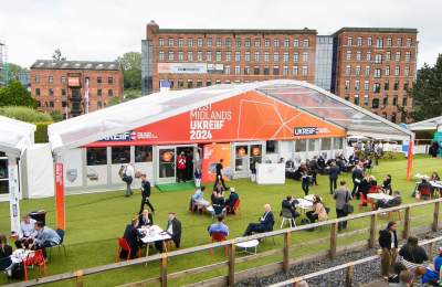 The outside of the West Midlands Pavilion at UKREiiF 2024. Guests network and enjoy a drink on the green in front of the stand.