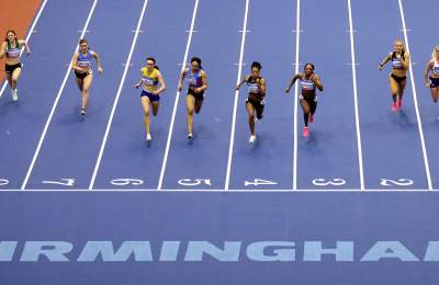 Eight runners race towards the camera on a blue running track with the Word BIRMINGHAM in bold letters at the end
