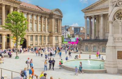 Groups of people sitting outside in summer clothes. Surrounded by Chamberlain Square fountain and Birmingham Museum and Art Gallery