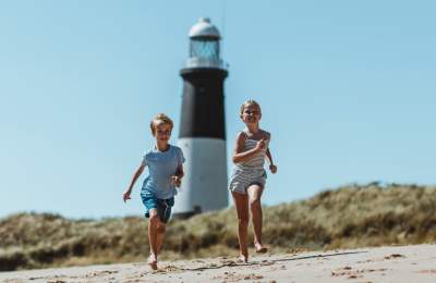 Two children run across the sand at Spurn Point in East Yorkshire with the iconic black and white lighthouse in the background