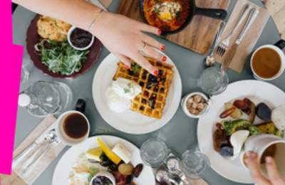 Overhead view of a shared brunch table with waffles, eggs, coffee, and breakfast dishes being served