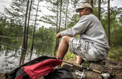 Man fishing along the shoreline at Carvers Creek State Park, surrounded by pine trees and calm water.