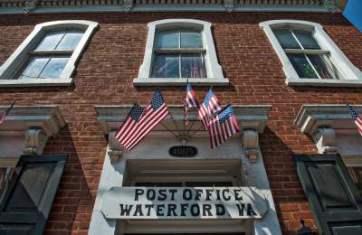 Historic brick Post Office building in Waterford, Virginia, decorated with American flags above the entrance.