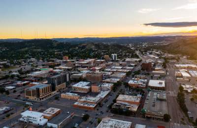 Aerial view of downtown Rapid City at sunset with the Black Hills stretching across the horizon.