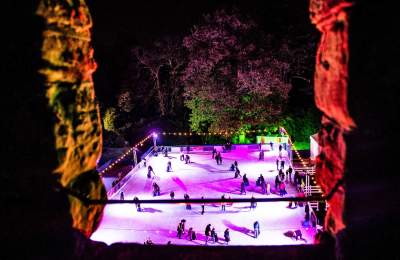 An outdoor ice rink through a castle window lit up with colourful lights