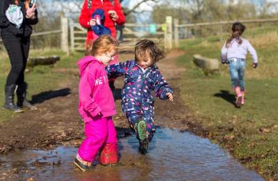 Two young children in brightly coloured winter clothes splashing in a muddy puddle