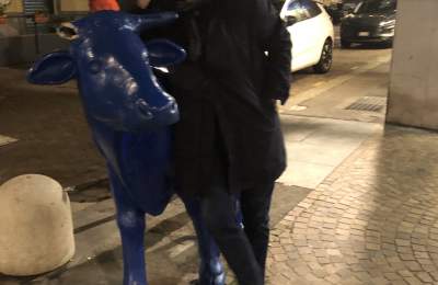 A man standing next to a statue of a blue cow on the street.