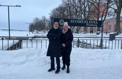 Two people pose in front of a sign during winter in Helsinki.