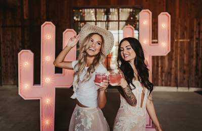 Two girls with drinks in front of pink light up cactus signs