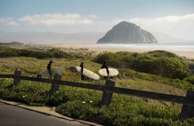 Three surfers with surf boards walking to the ocean with Morro Rock in the background