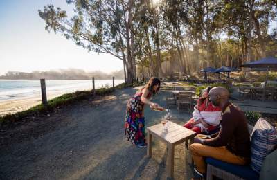 Couple wine tasting outside next to the beach with sun coming through eucalyptus trees
