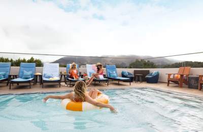 Person in an inner-tube in a pool with beach chairs and mountain in the background