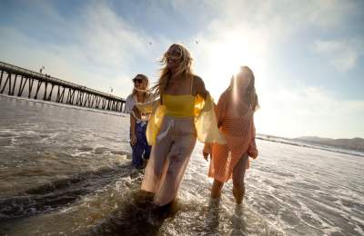 Three women walking through water near Pismo Pier with sun in background