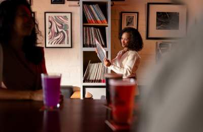 Women at bar looking at records in the background with other people in foreground with drinks