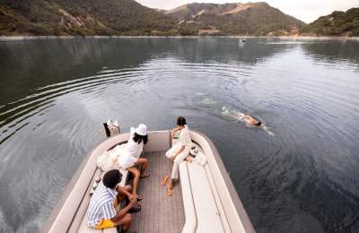 Three people in a pontoon boat watching one person swim alongside the boat in a lake