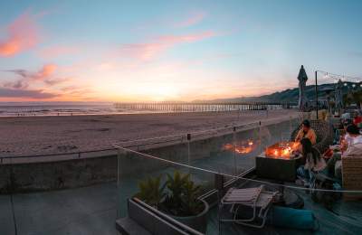 People watching sunset on a patio overlooking the beach with a firepit