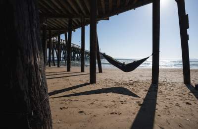 Person reading in a hammock under a pier next to the ocean